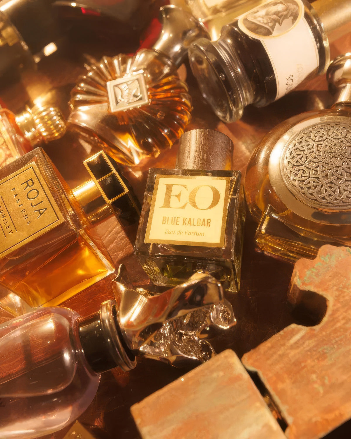 Ensar Oud Blue Kalbar bottle nestled among golden niche flacons on wood, floral oud extrait decant