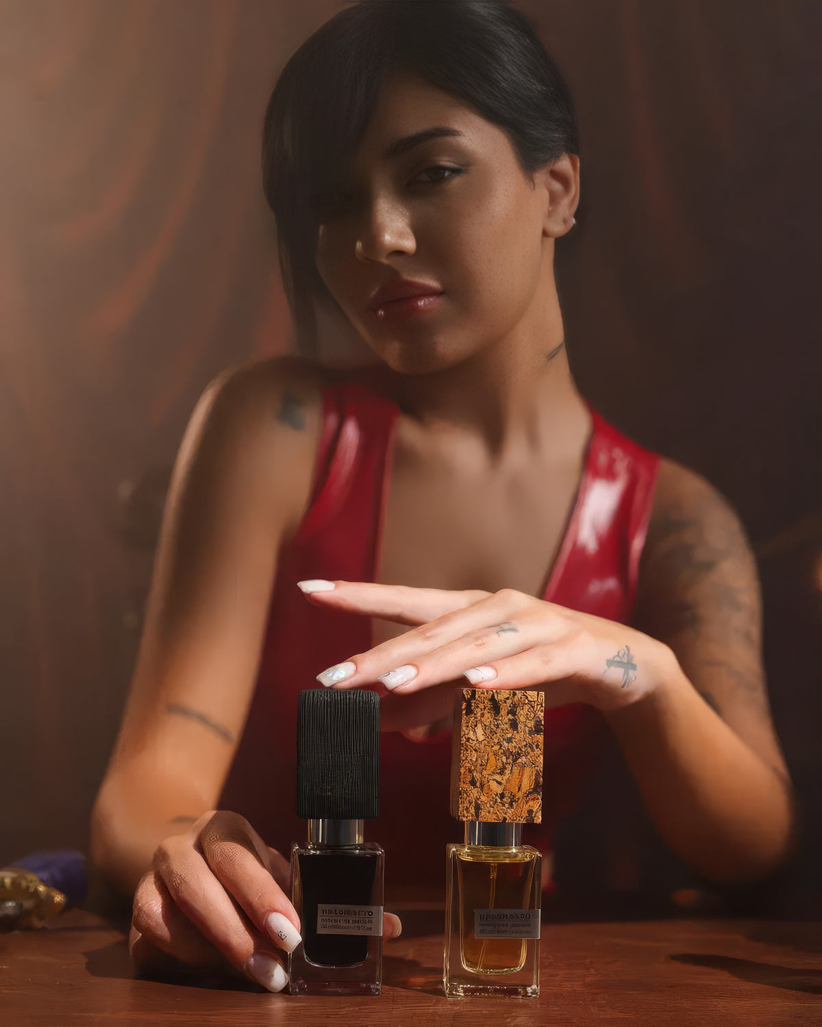 Nasomatto Baraonda flacon on a table beneath a woman in red resting her hand over it, boozy amber niche fragrance decant