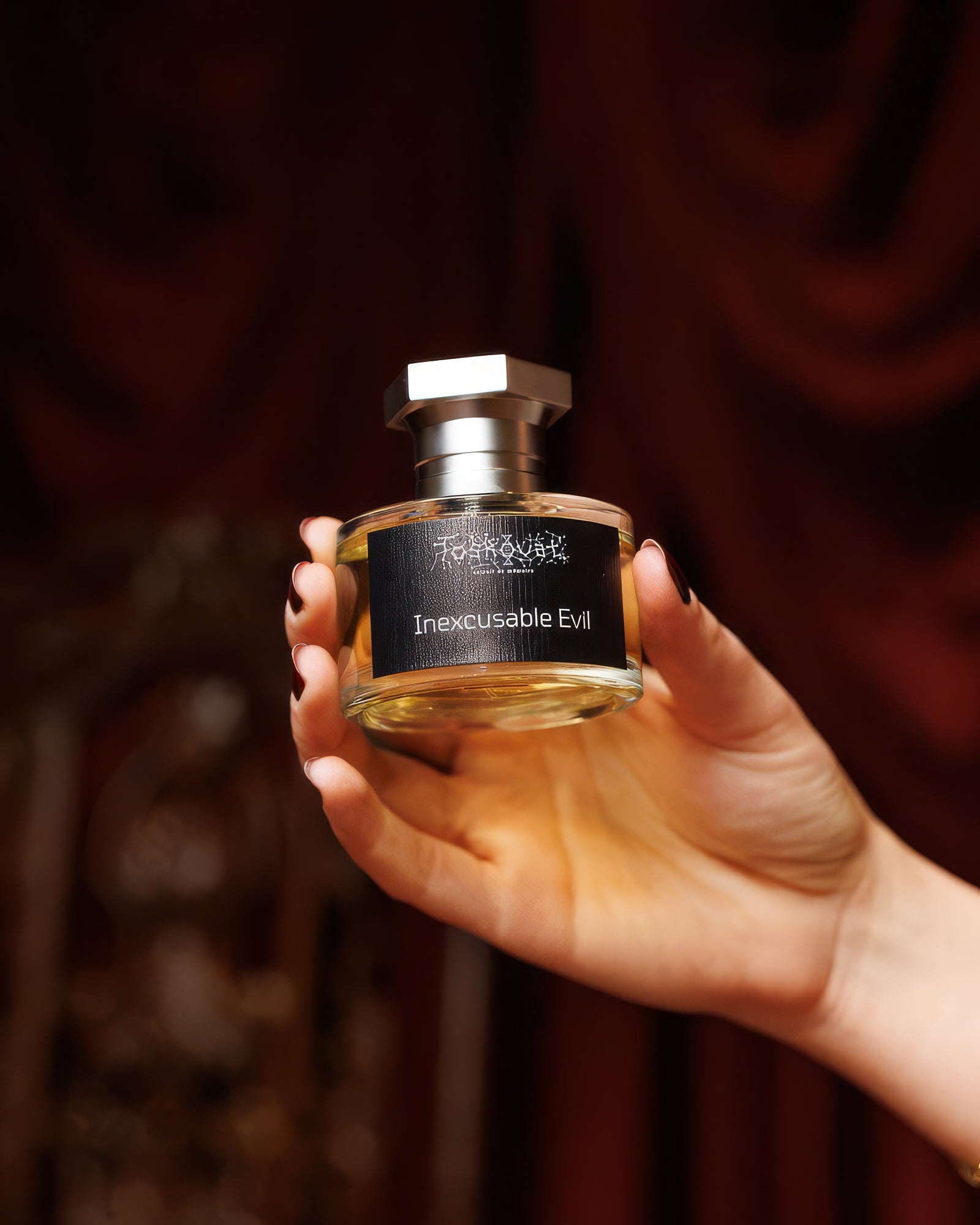 Hand hält den Toskovat Inexcusable Evil Flakon vor tiefrotem Samt, dunkles rauchiges Extrait-de-Parfum-Sample
