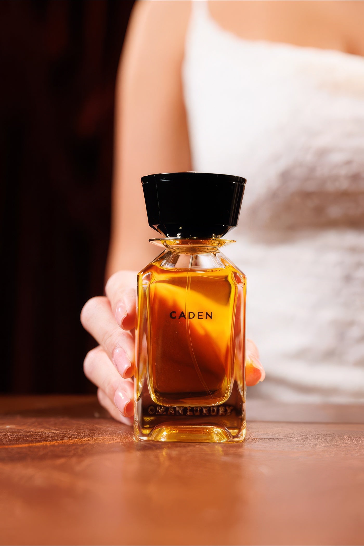 Oman Luxury Caden flacon held close on a warm wooden table, model in a white top, oud niche perfume sample