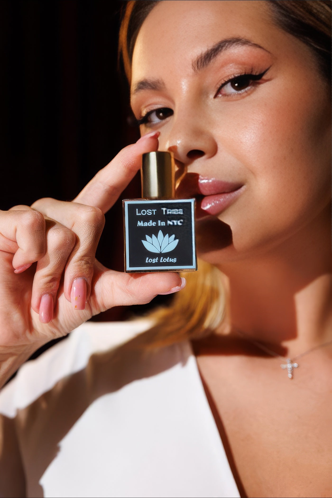 Boccetta Lost Tribe Lost Lotus accostata al viso di una modella in luce calda, campione di eau de parfum acquatica