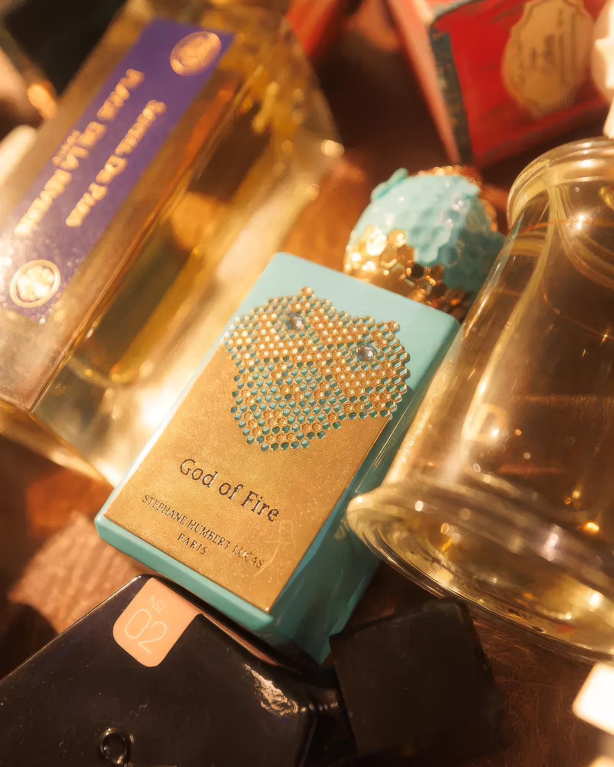 Stephane Humbert Lucas 777 God of Fire قارورة على طاولة بإضاءة ذهبية دافئة بين الزجاجات، عينة عطر فاكهي بالعود