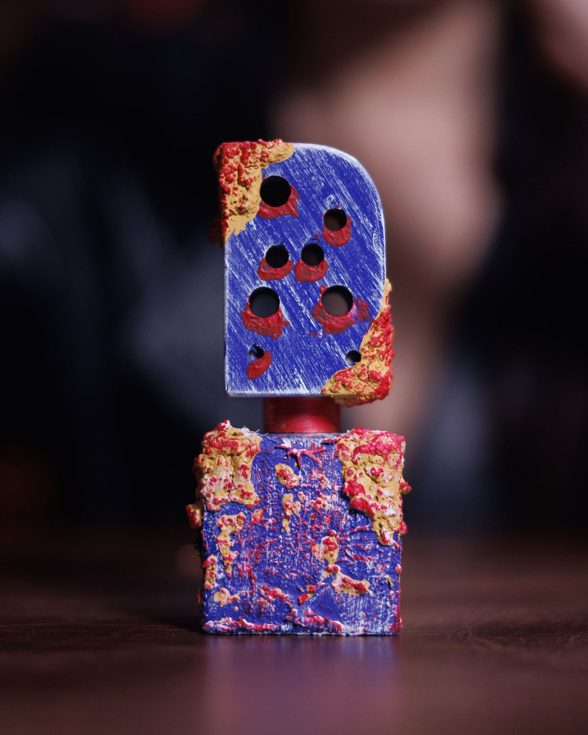 Flacone blu Adi Ale Van Hai Hui, tappo traforato da fori bordati di rosso, su legno scuro con una figura sfocata sullo sfondo, decant di extrait de parfum resinoso