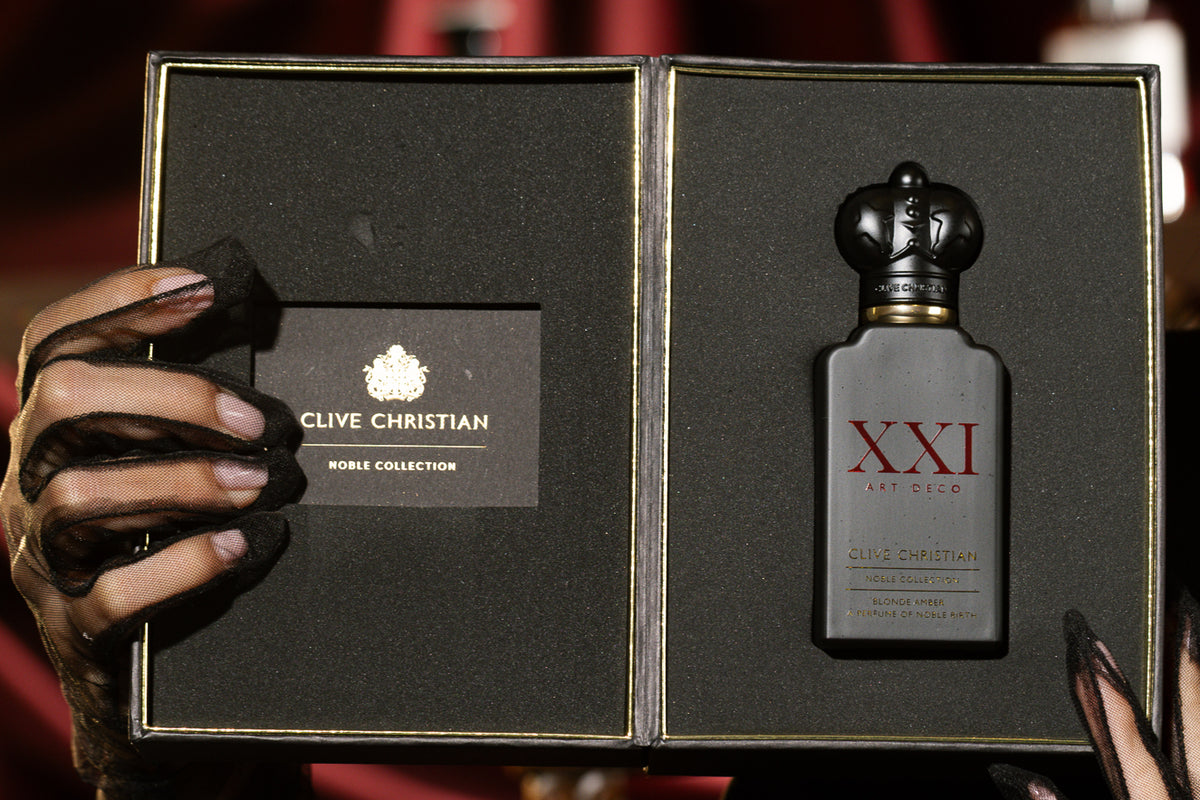 Clive Christian XXI Art Deco Blonde Amber, the crown-capped bottle in its black presentation case held open by sheer black-gloved hands
