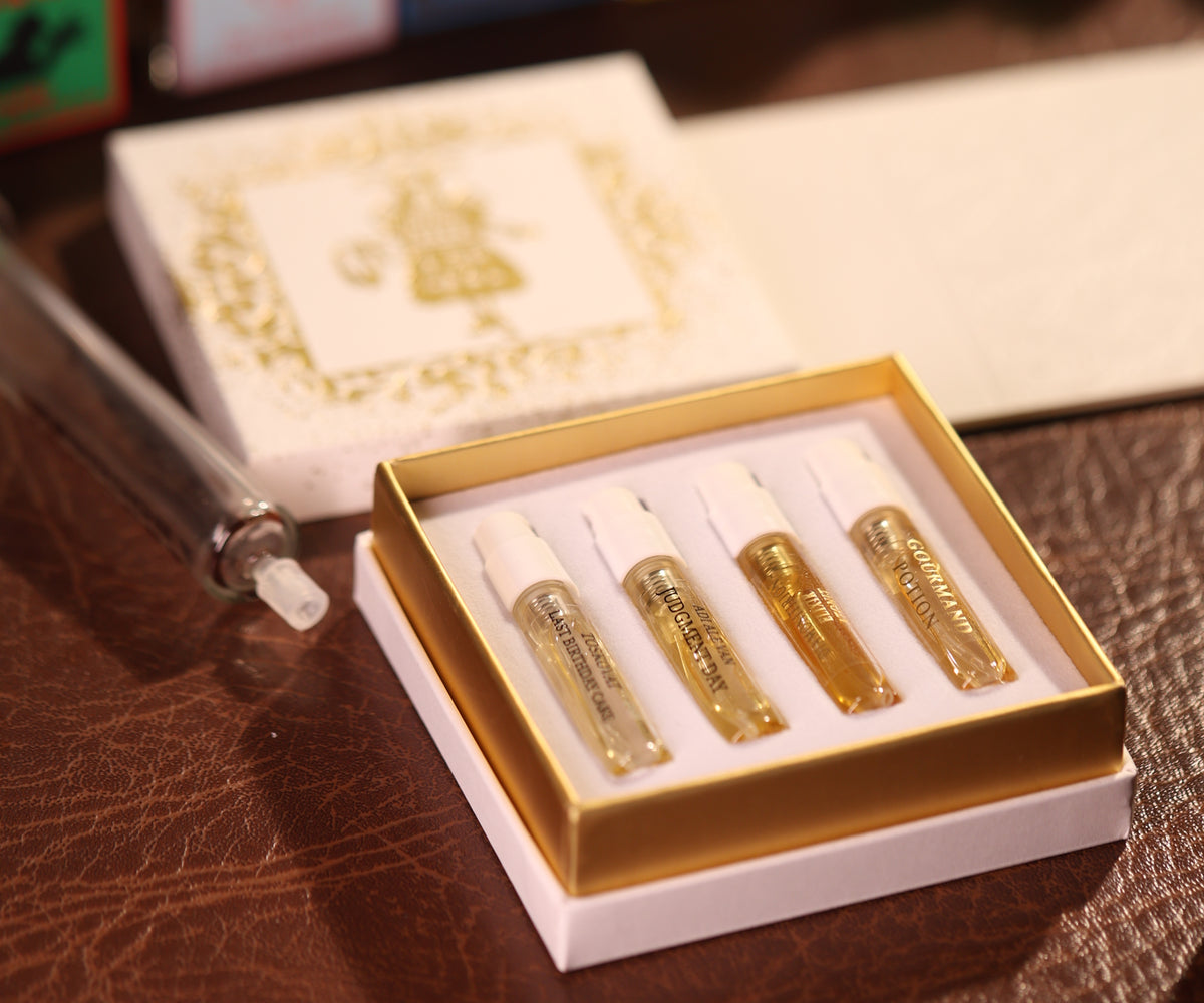 Open Gouttes Rares discovery box with four 2 ml sample sprays in a gold tray, its gold-printed figure lid and a glass syringe beside it on brown leather
