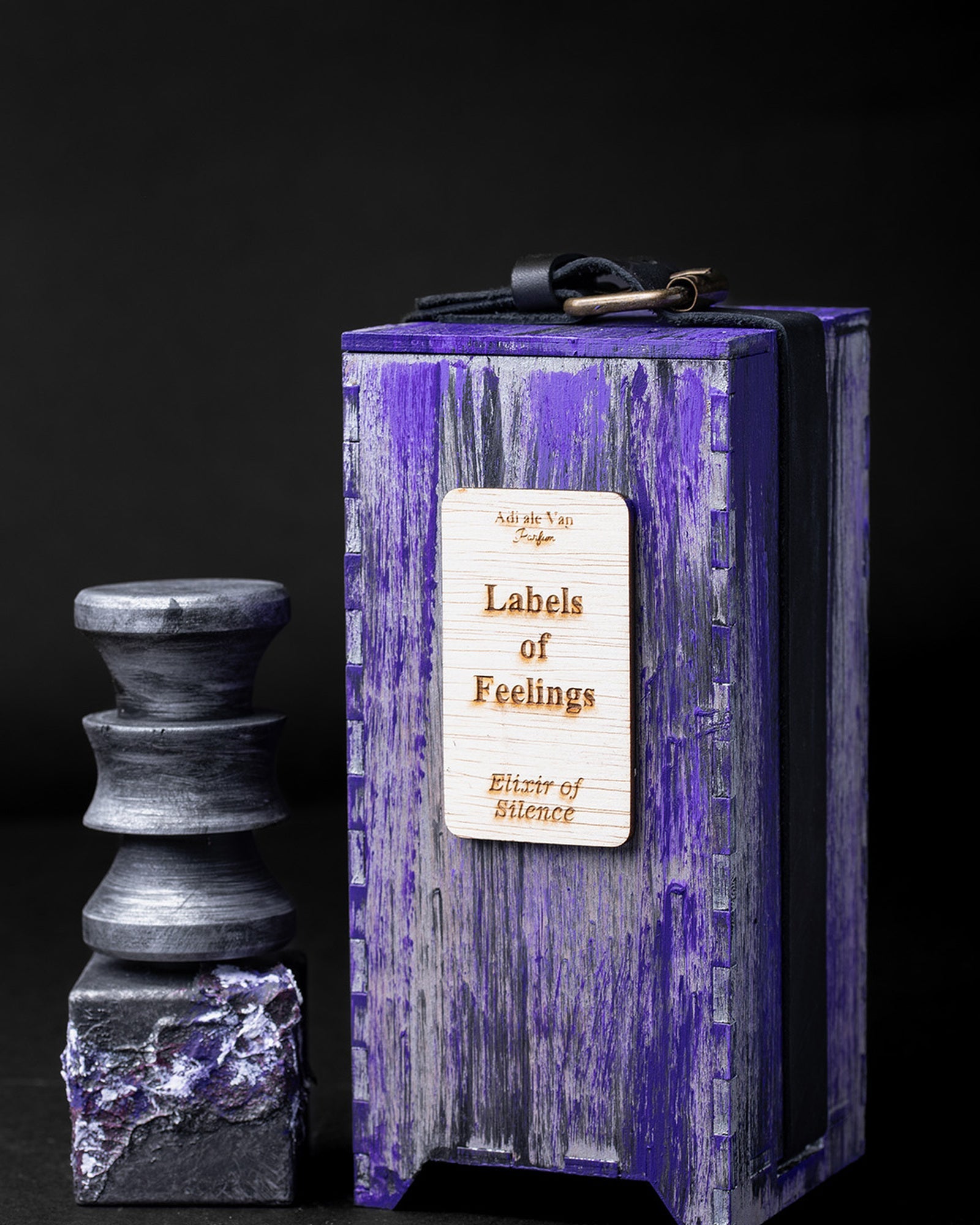 The Labels of Feelings object beside its hand-painted violet wooden box and printed label, lit against black.
