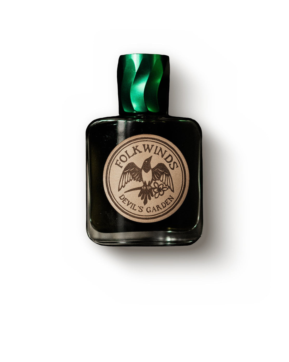 Folkwinds Devil's Garden, front view: a square glass bottle of dark green juice with a twisted green cap and a round copper label showing a bird, Folkwinds and Devil's Garden.
