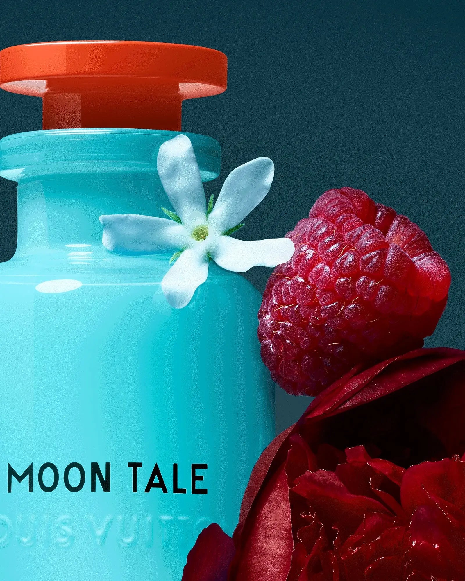 A close view of the turquoise Moon Tale flacon against deep teal, a single white jasmine flower and a raspberry resting at its shoulder.