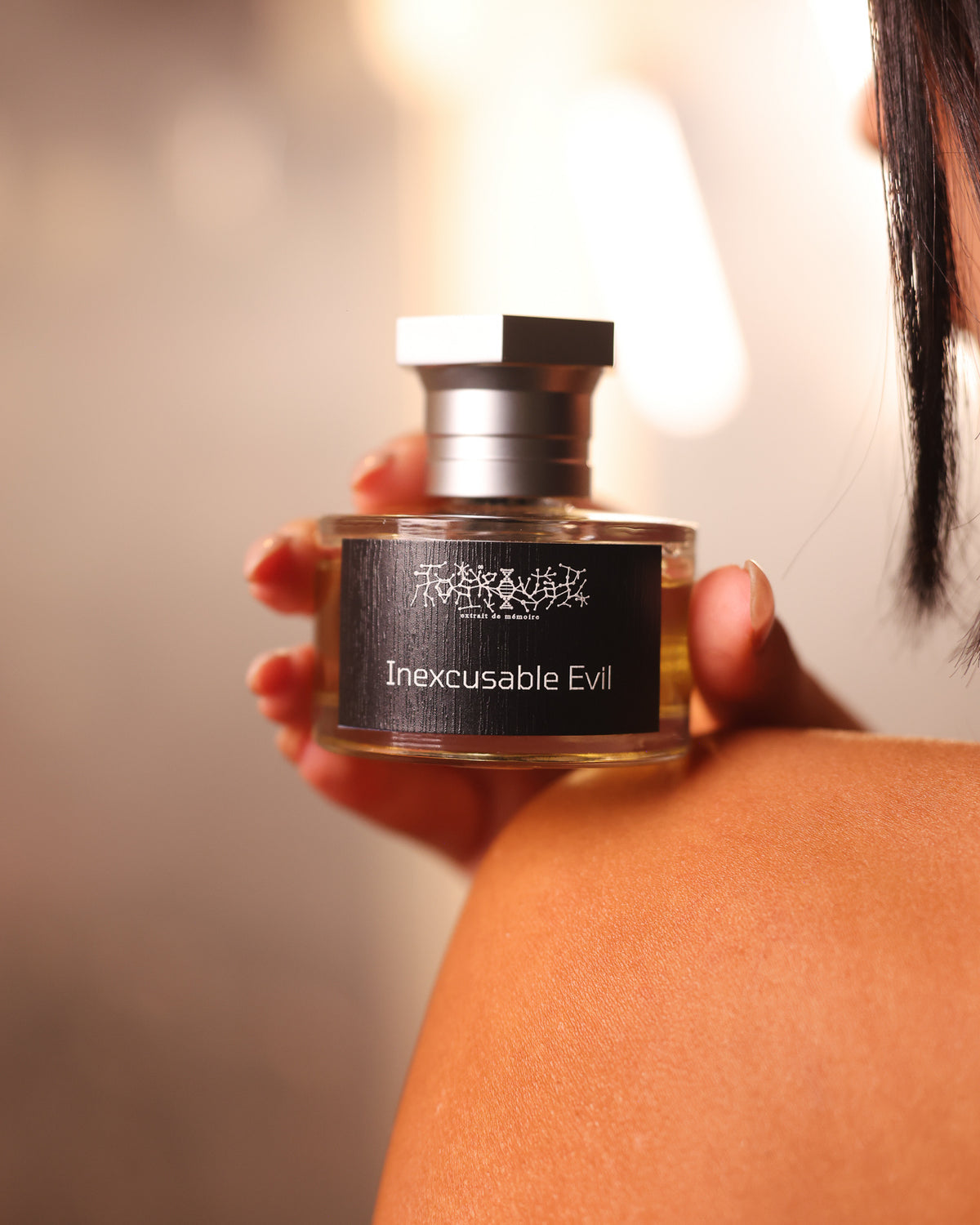 Toskovat Inexcusable Evil, flacon posé sur une épaule nue près d'une chevelure sombre sur un flou doux et chaleureux, décant de parfum de niche sombre et fumé