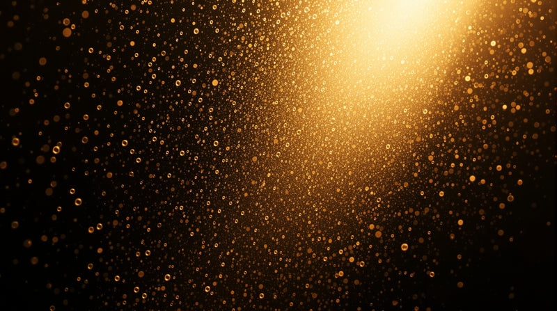 A fine suspended mist of golden droplets caught in a shaft of warm light against deep shadow