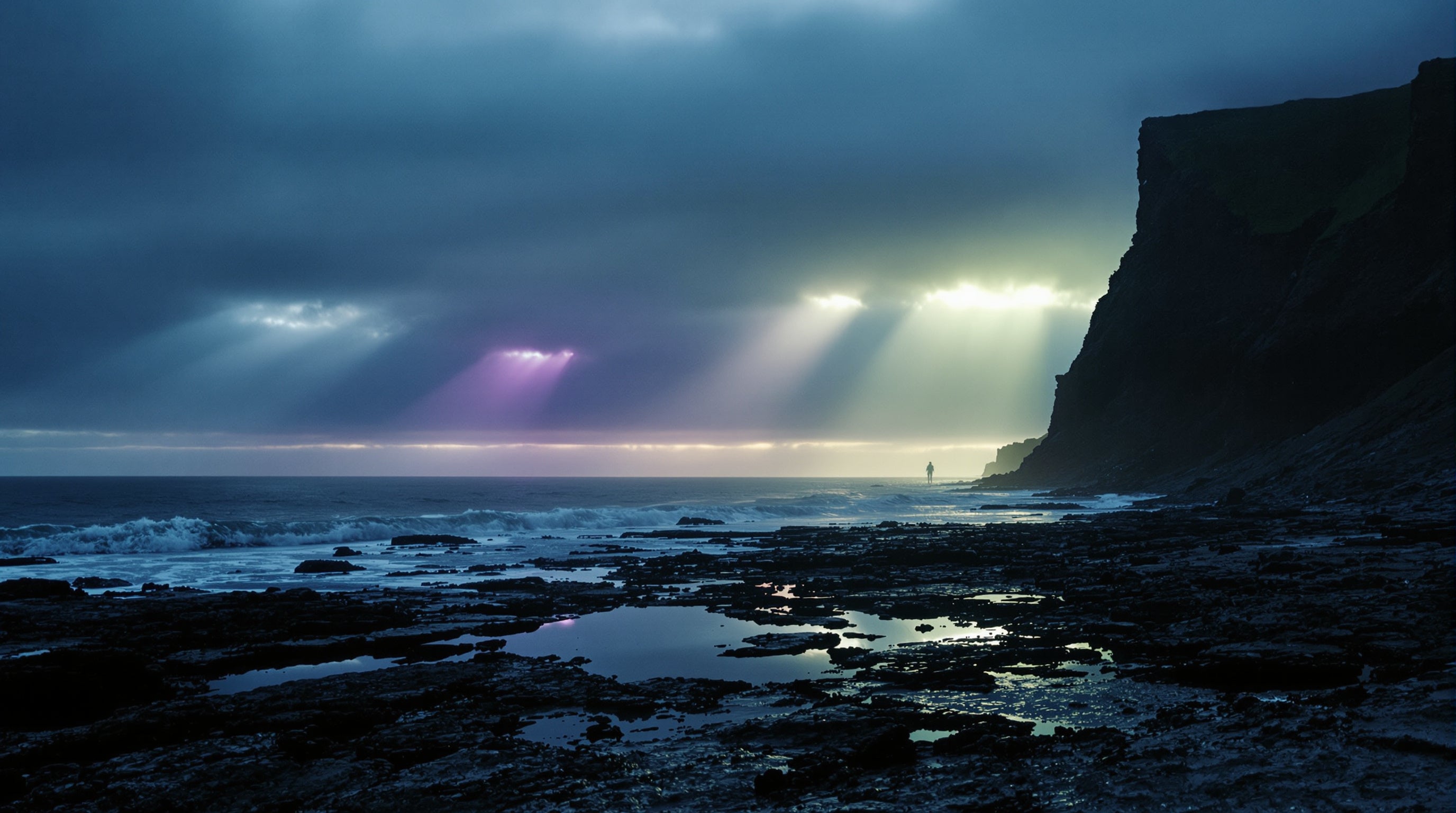Shafts of coloured light breaking through cloud onto wet black coastal rock and tide pools at dusk