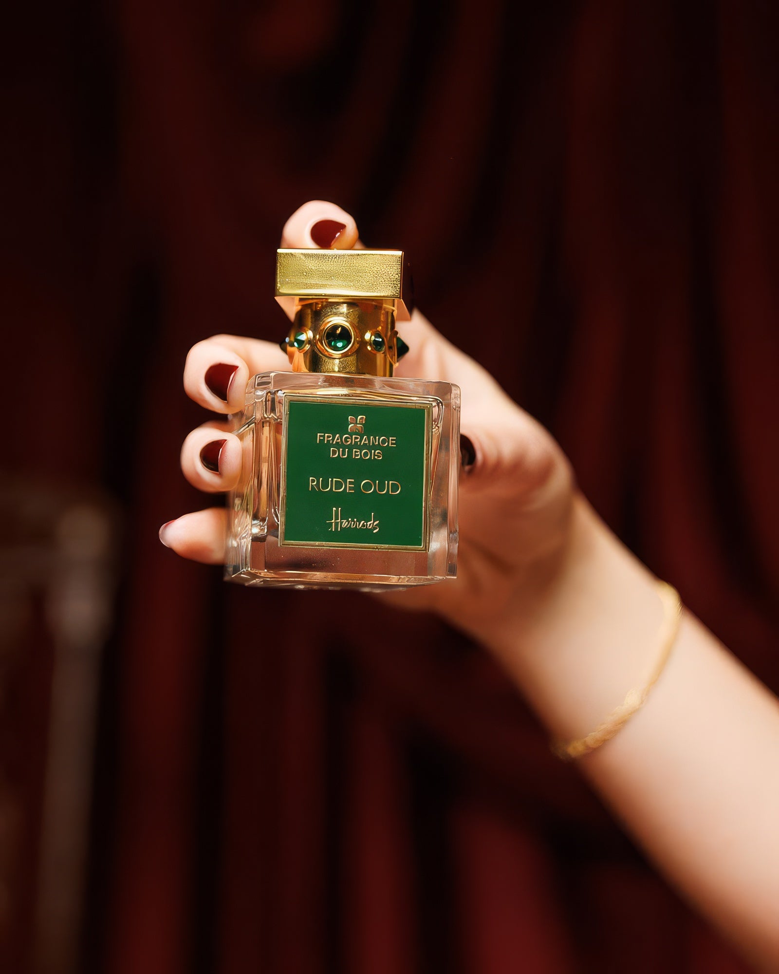 Fragrance Du Bois Rude Oud tenu dans une main soignée sur velours bordeaux, décant de parfum niche oud cuiré