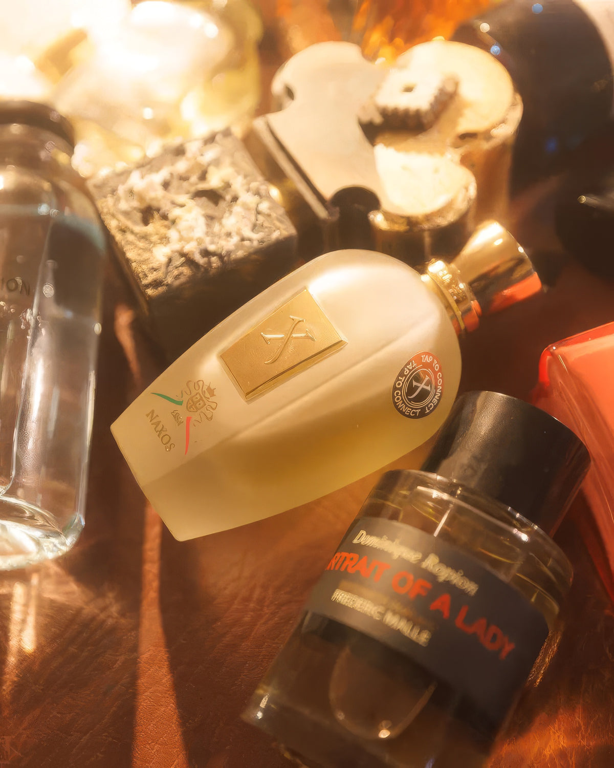 Xerjoff Naxos laid among other flacons in warm candlelight, tobacco vanilla gourmand fragrance sample