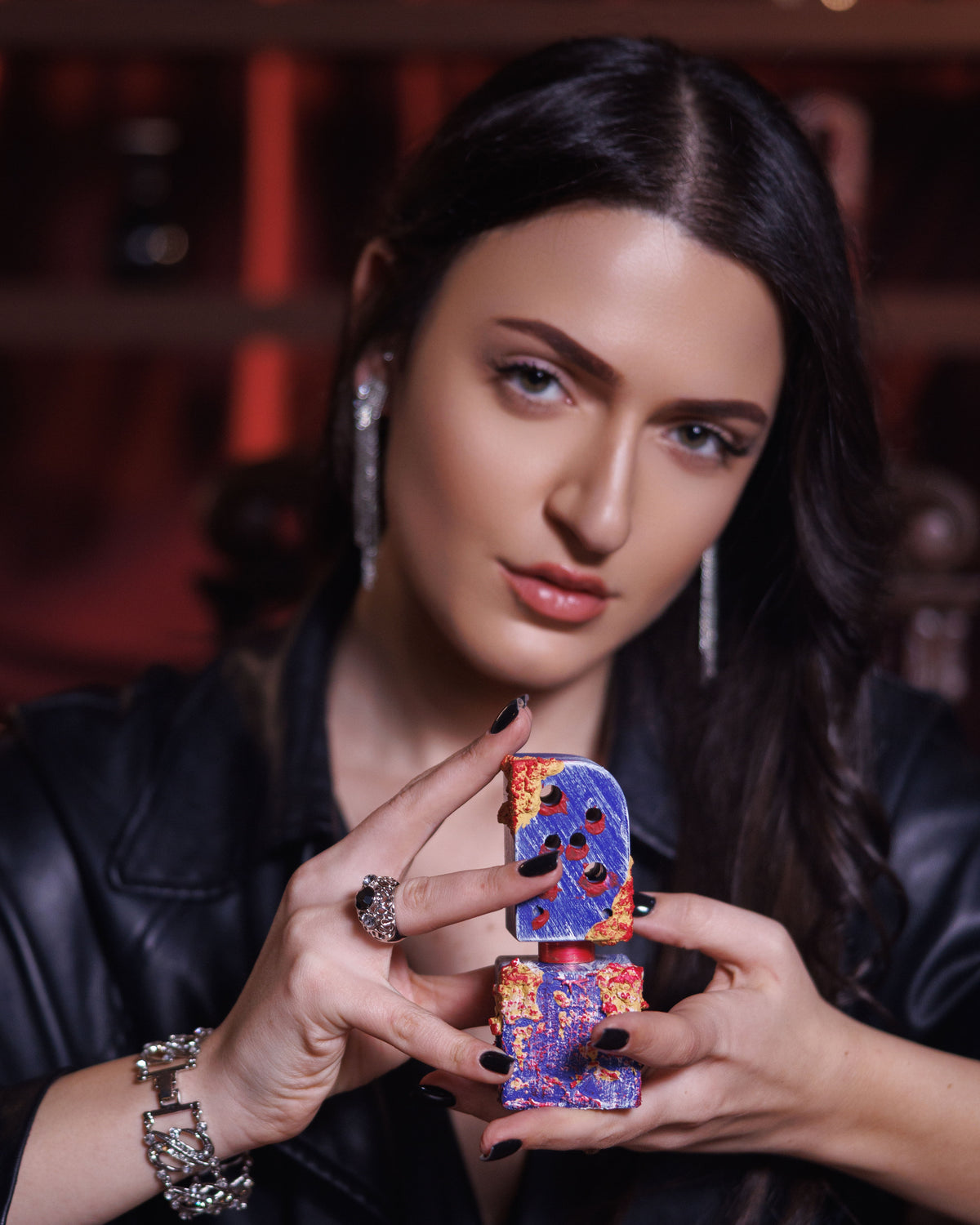 Flacone Adi Ale Van Hai Hui tenuto dritto tra le punte delle dita con unghie nere da una donna in giacca di pelle e orecchini di cristallo, decant di extrait de parfum resinoso