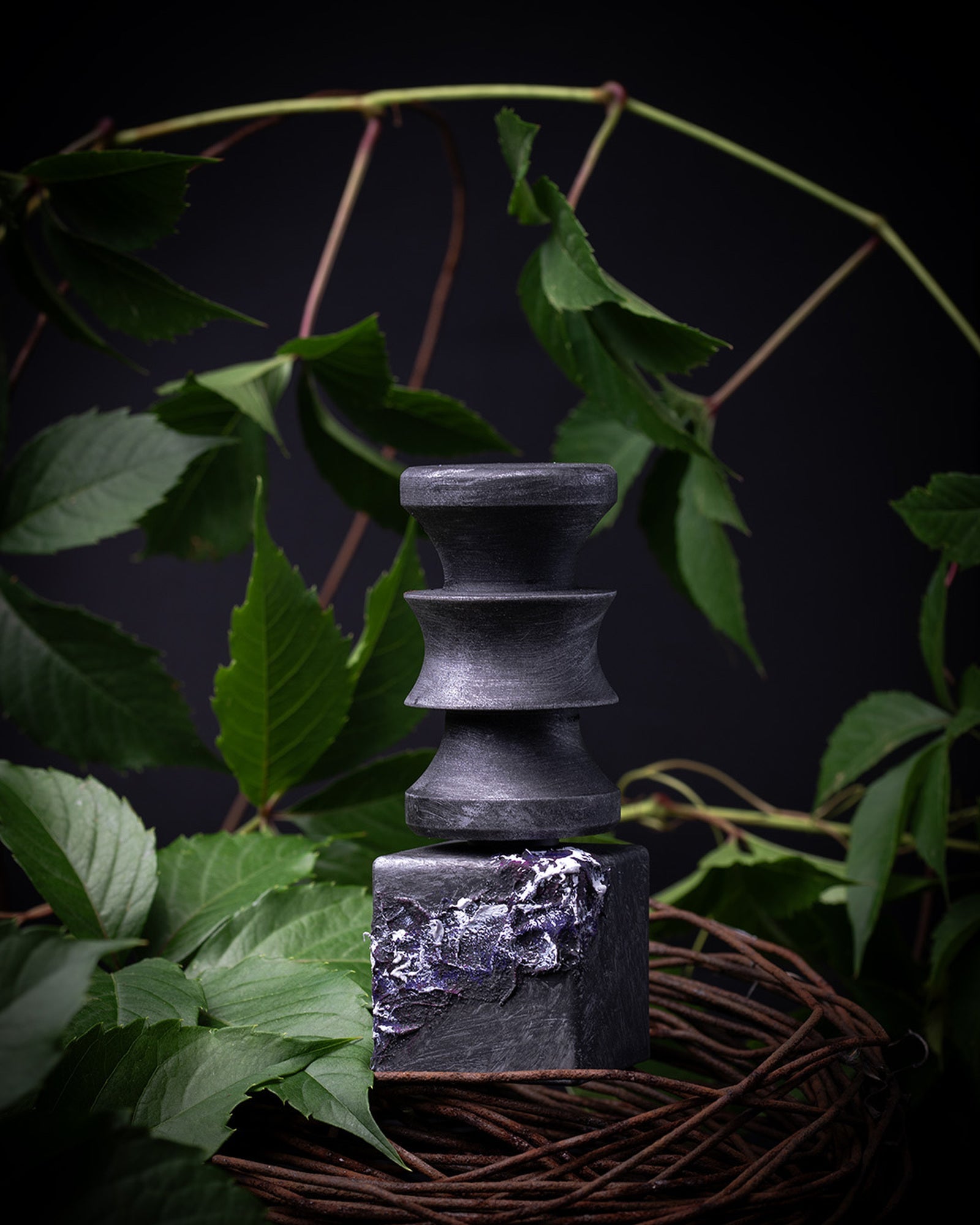 The Labels of Feelings turned-wood stack among green foliage and a coiled vine, lit against black.