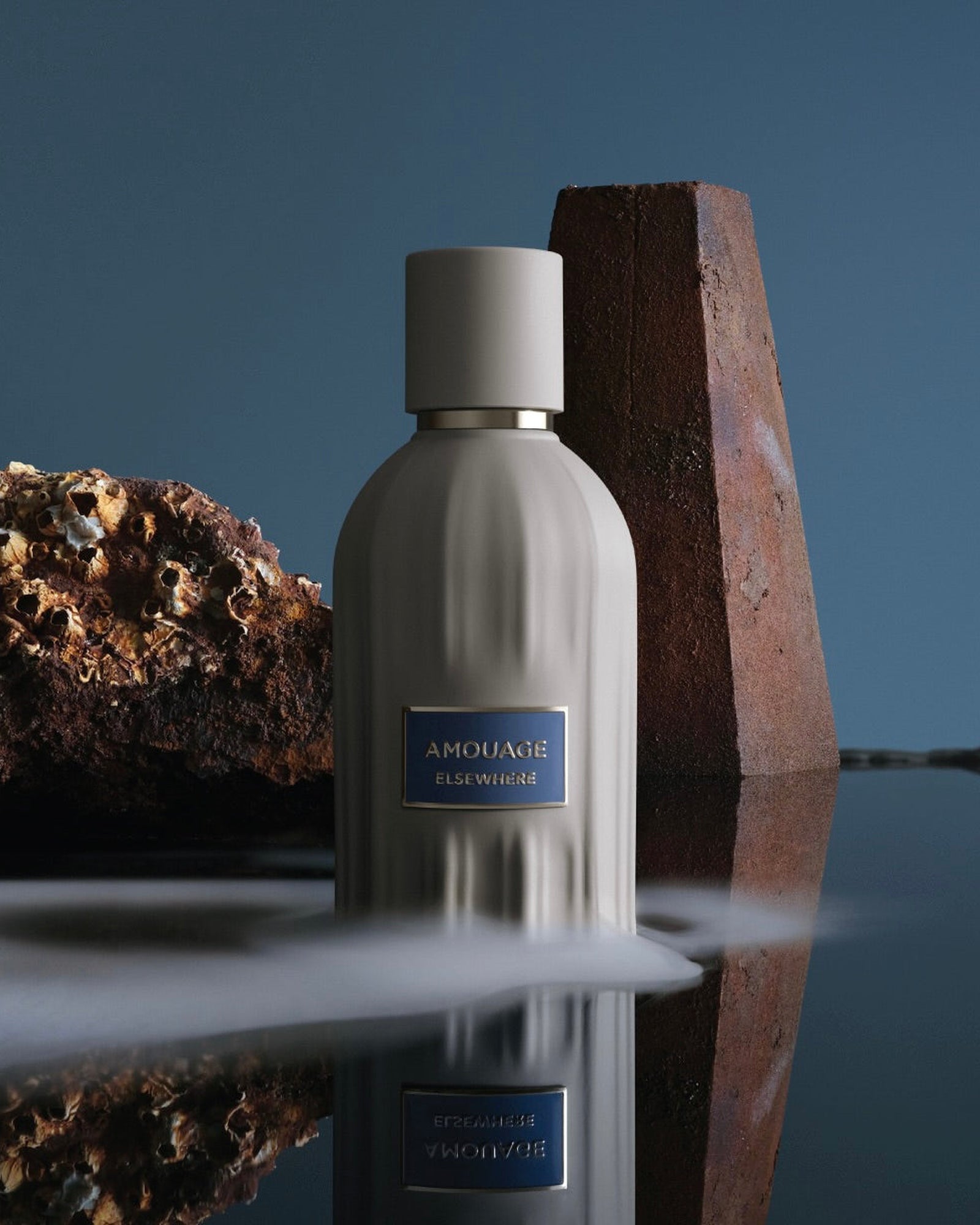 The Elsewhere flacon in a still life against a rust-coloured stone slab, low mist drifting over dark reflective water.