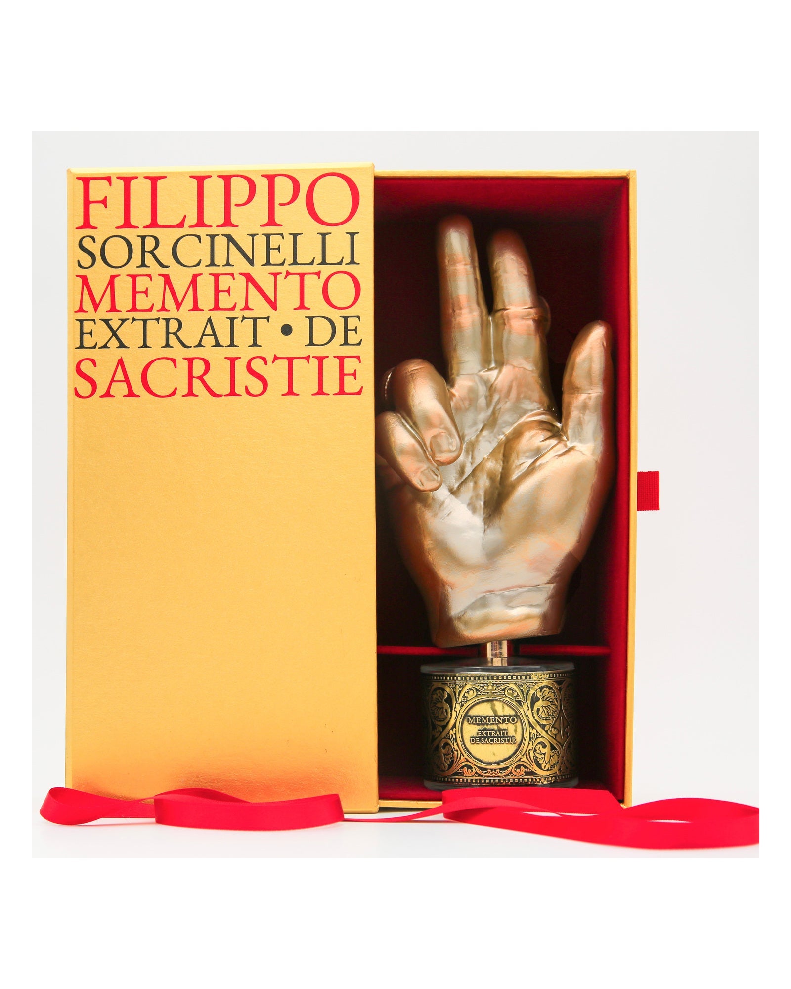 The open MEMENTO presentation box for Sacristie Des Arbres, its orange sleeve printed with the collection name and the gilded hand flacon seated inside.