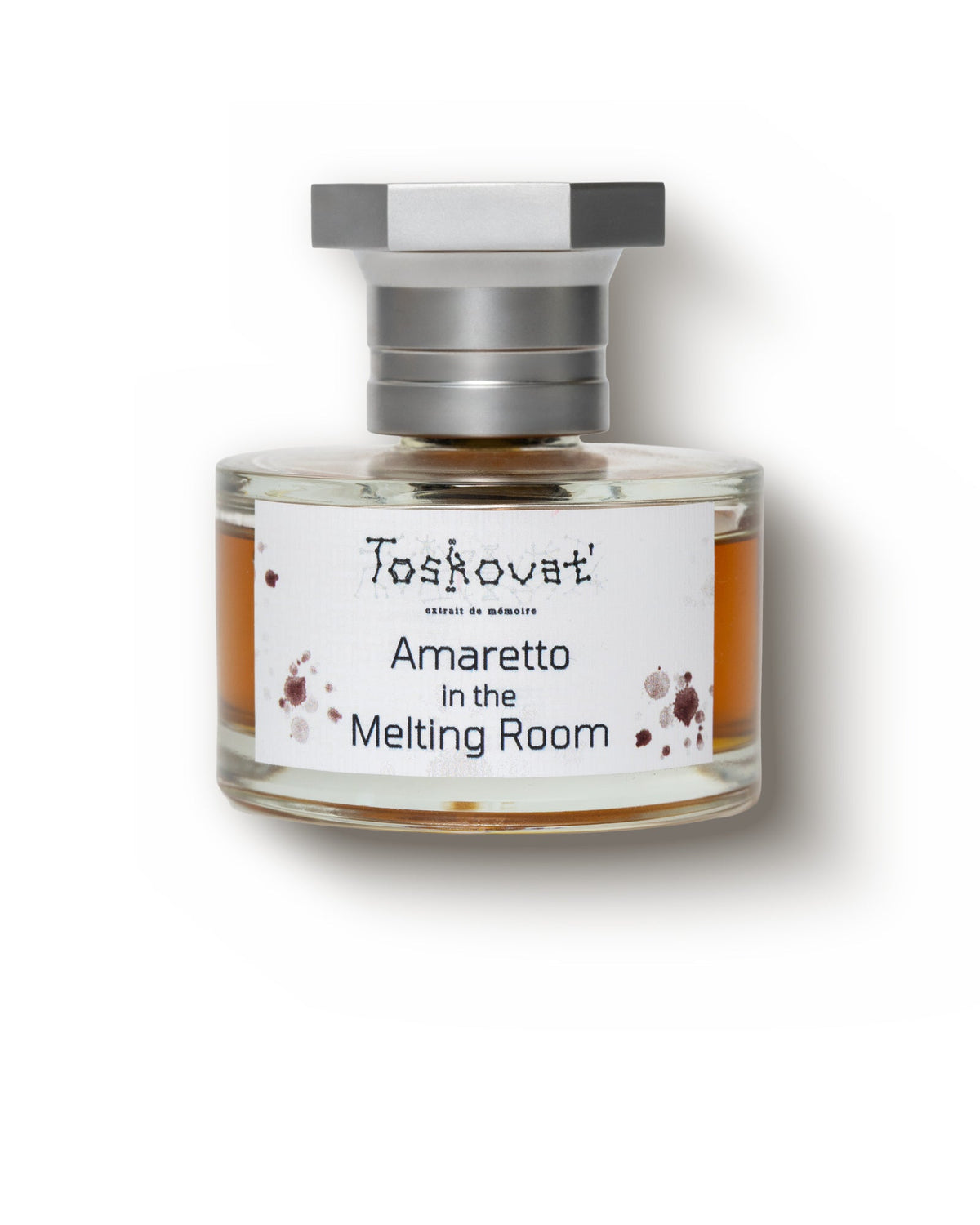 Toskovat Amaretto in the Melting Room, front view: a round clear bottle of amber juice under a hexagonal steel cap, its white label printed Amaretto in the Melting Room among dark red splashes.