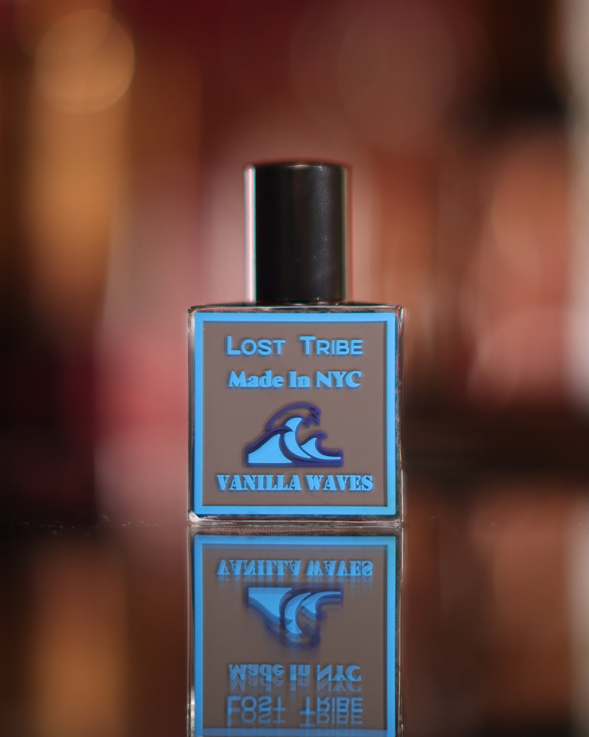 Bottiglia quadrata Lost Tribe Vanilla Waves V2 Extra Musk, tappo nero e onda blu su etichetta tortora, riflessa in uno specchio scuro, decant di profumo gourmand alla vaniglia
