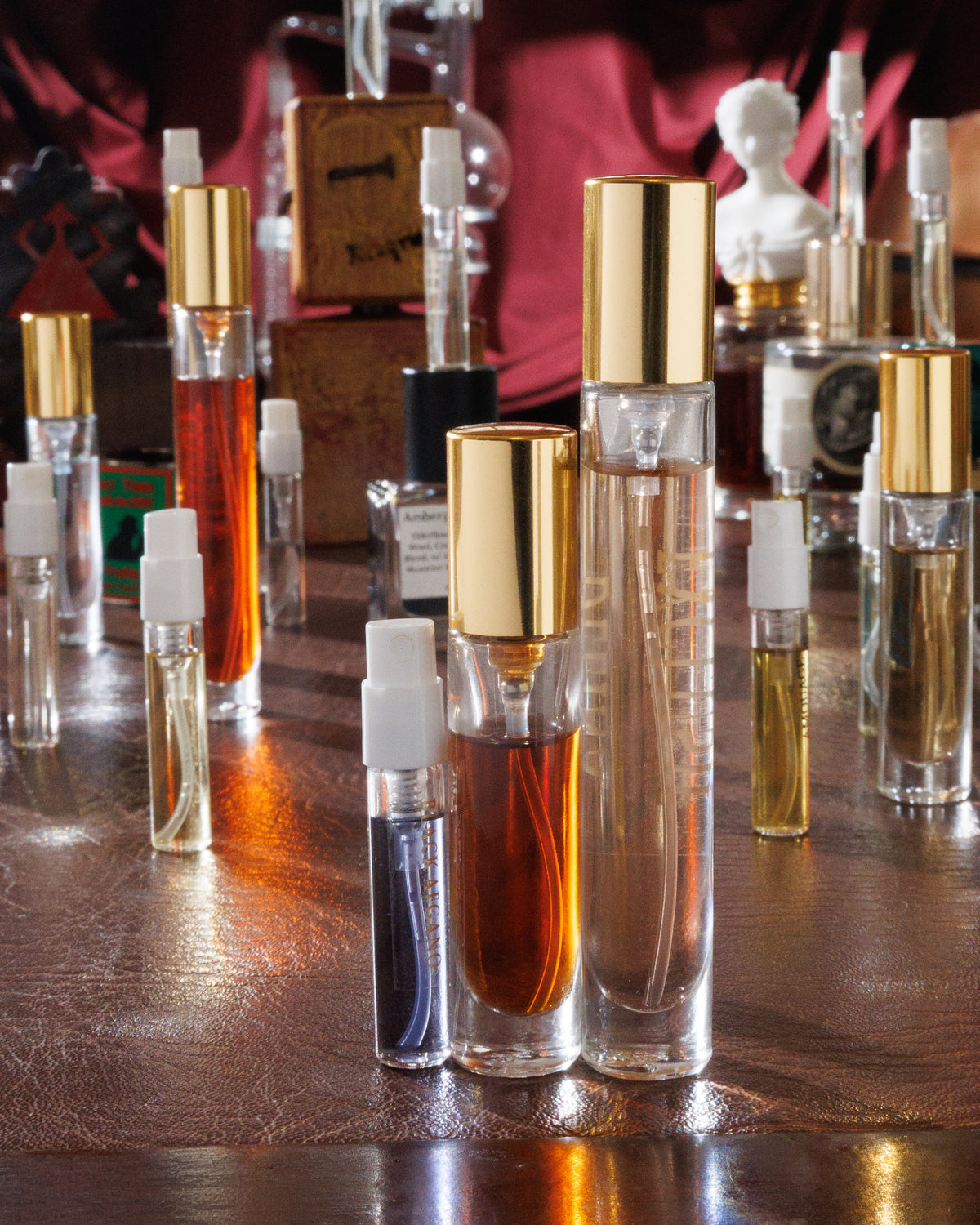 Parfums de Marly Delina Exclusif als 10-ml-Abfüllung mit goldener Kappe, daneben ein 5-ml-Zerstäuber und eine 2-ml-Probe Black Afgano auf einem Lederschreibtisch, Nischenparfum-Abfüllung