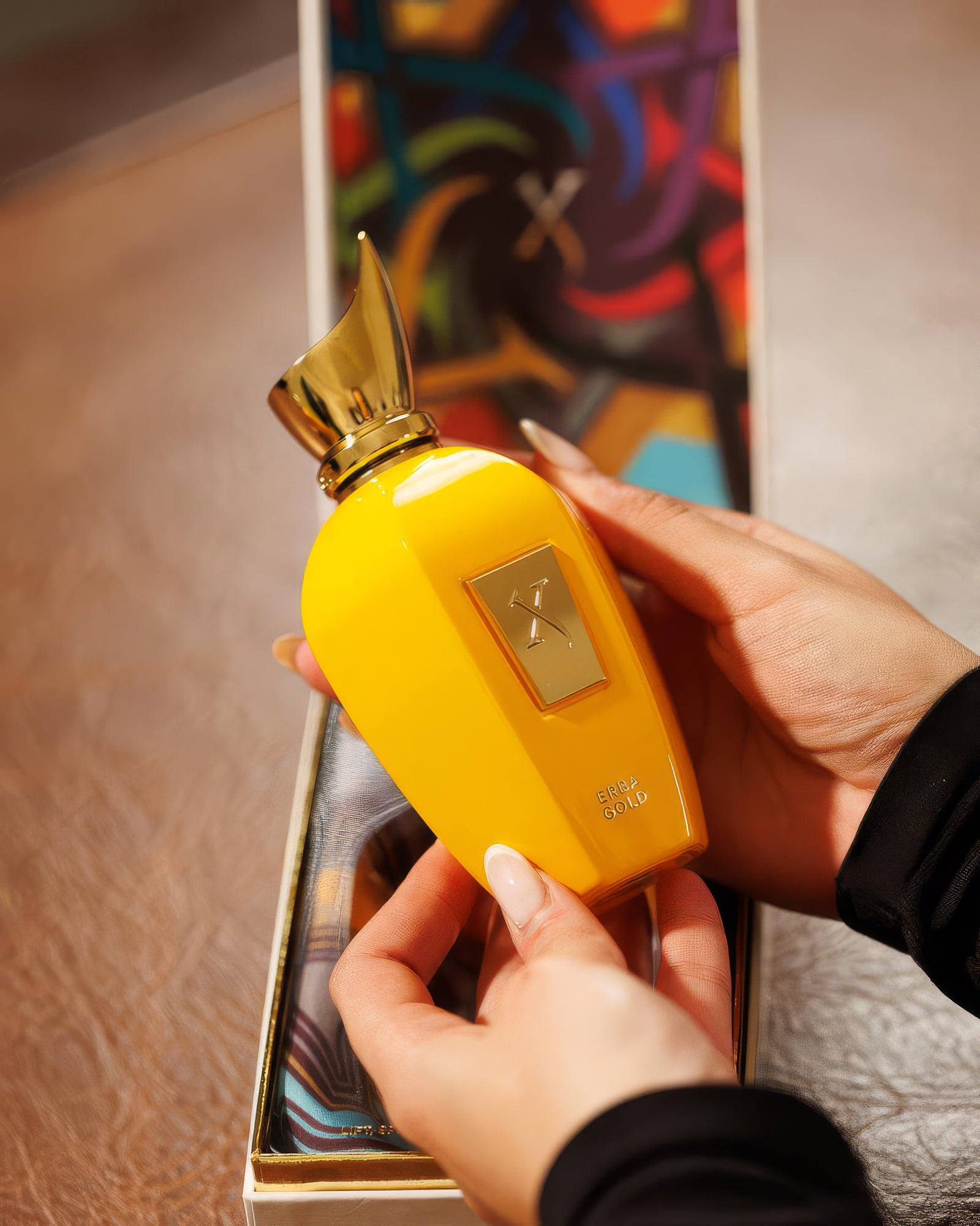 Hands cradling the Xerjoff Erba Gold bottle over its colorful printed box, aromatic citrus fragrance decant