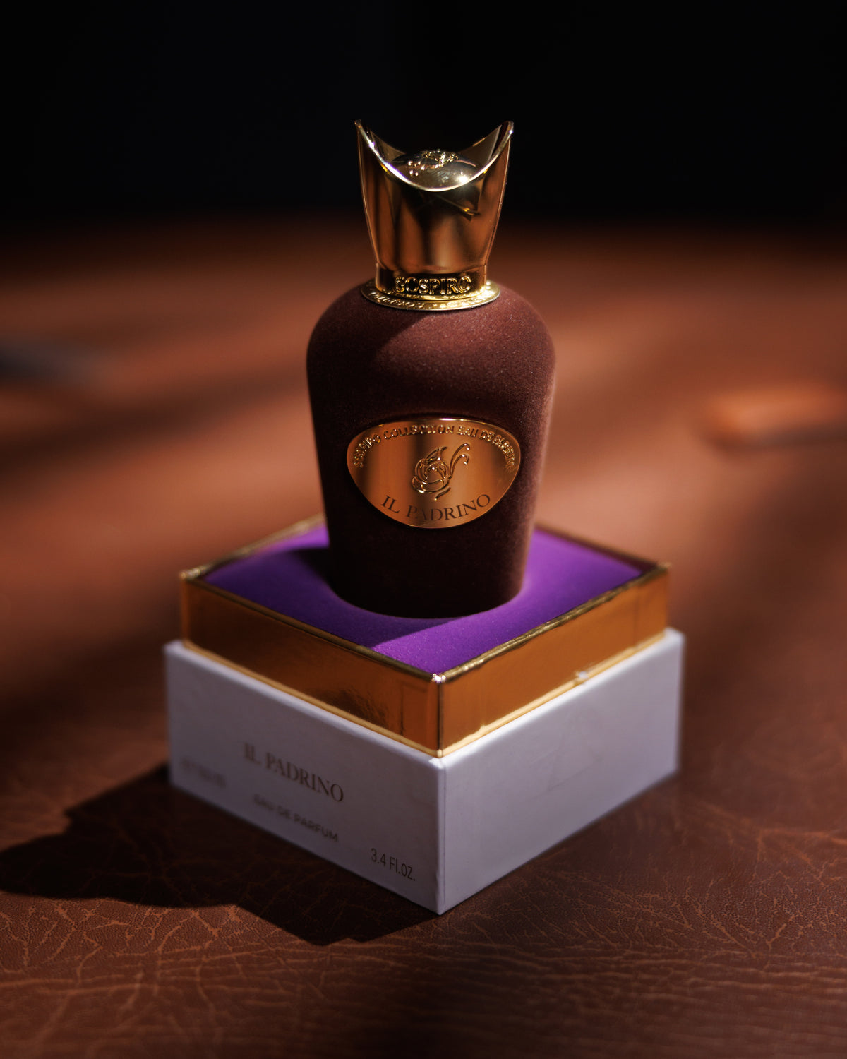 Sospiro Il Padrino Flasche in braunem Samt mit goldener Kronenkappe, stehend in ihrer offenen Schachtel, violetter Samteinsatz auf dunklem, rissigem Leder, Abfüllung eines holzigen Amber-Nischenparfums